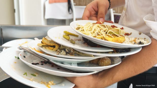 Photo d'un serveur portant des assiettes pleines de restes alimentaires. Crédit photo : Adobe Stock © kpn1968